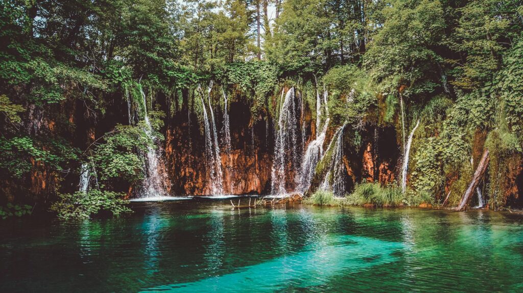 amazing waterfall flowing through rocky cliff with green trees on sunny day